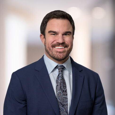 A man in a navy suit, light blue shirt, and patterned tie stands smiling in a blurred indoor setting, reflecting the professionalism of top lawyers in Chicago.