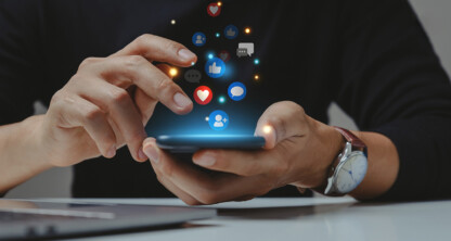 Person using a smartphone with social media icons like likes, hearts, and comments appearing above the screen. A laptop is visible on the table—perfect for chicago lawyers staying connected or working on intellectual property law cases.