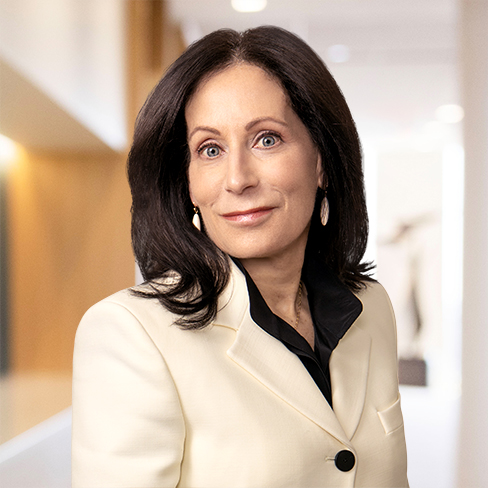 A woman with long dark hair wearing a cream-colored blazer and black blouse stands in a well-lit corporate law office hallway, looking at the camera—reflecting the professionalism of top lawyers in Chicago.