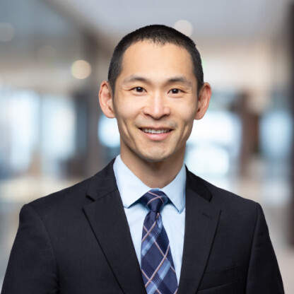 A man wearing a dark suit, light blue shirt, and patterned tie stands indoors against a blurred office background, facing the camera and smiling—representing the professionalism of top lawyers in Chicago.