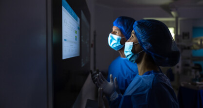 Two medical professionals in scrubs and masks review data on a large screen in a dimly lit hospital, much like lawyers in Chicago analyzing critical information for litigation support.