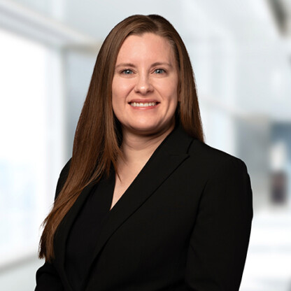 A woman with long brown hair, wearing a black blazer, stands in front of a blurred office background, smiling at the camera—representing litigation support offered by leading lawyers in Chicago.