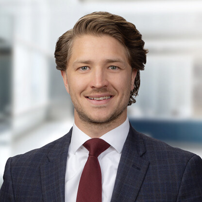 A man in a blue plaid suit, white shirt, and red tie smiles at the camera in a bright, modern corporate law office.