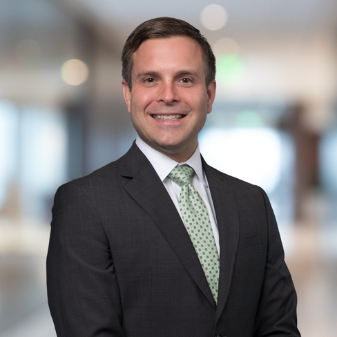 A man in a dark suit and green patterned tie smiles while standing in a blurred, modern office setting, reflecting the professionalism of top Chicago lawyers.