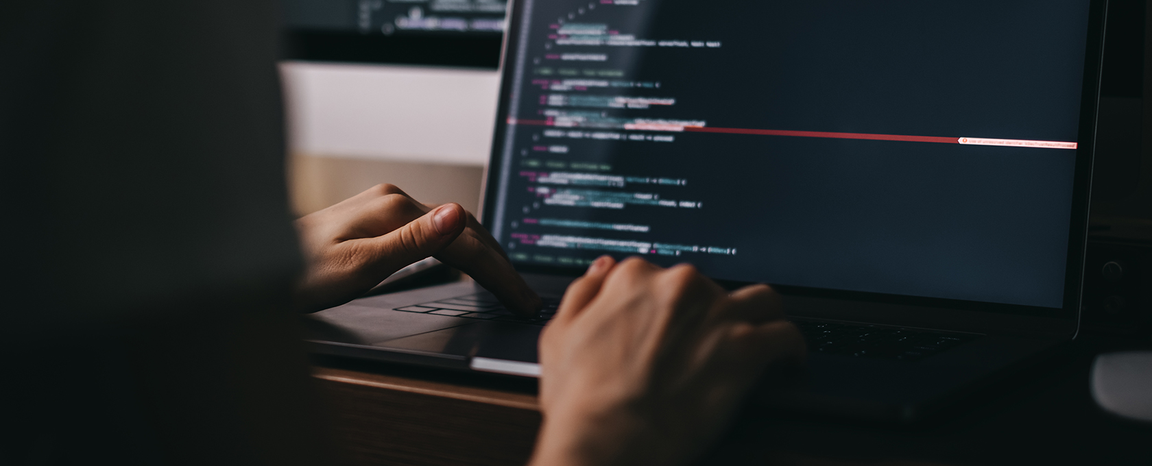 Person typing on a laptop displaying lines of code on a dark-themed screen in a dimly lit law office, highlighting the intersection of technology and intellectual property law.