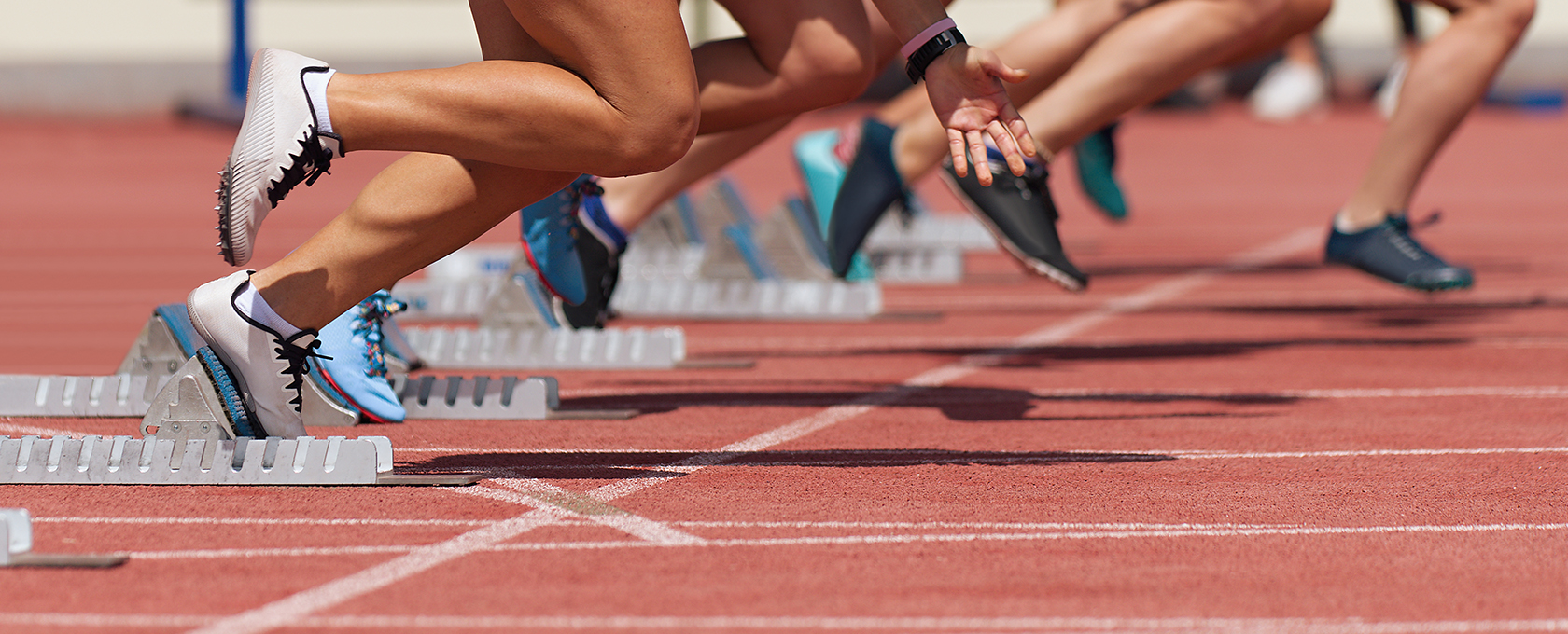 Sprinters in athletic gear launch from starting blocks on a red track, captured in mid-motion at the beginning of a race—much like Chicago lawyers springing into action to provide top-notch litigation support.