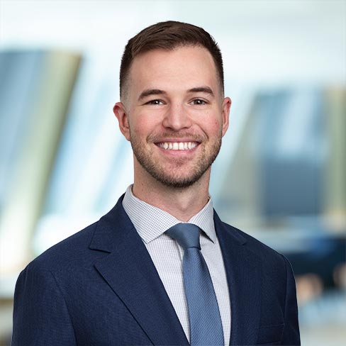 A man in a blue suit and tie smiles at the camera, standing in front of a blurred corporate law office, representing chicago lawyers dedicated to success.