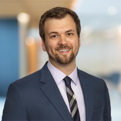 A man in a suit and tie stands in front of a blurred office background, smiling at the camera—representing one of the leading law offices for Chicago lawyers.