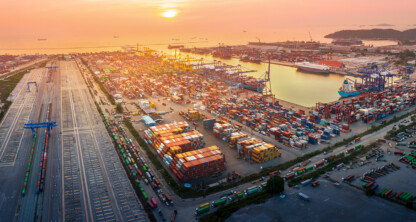 Aerial view of a busy shipping port at sunset, showing rows of colorful shipping containers, cranes, trains, and docked ships—much like the organized efficiency found in top law offices specializing in intellectual property law.