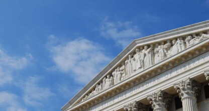 The top portion of a classical government building with columns and sculpted figures, reminiscent of law offices specializing in intellectual property law, set against a blue sky with scattered clouds.