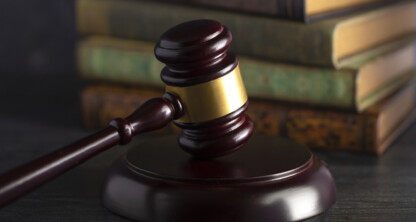 A judge’s gavel rests on a block in front of a stack of old law books on a dark surface.