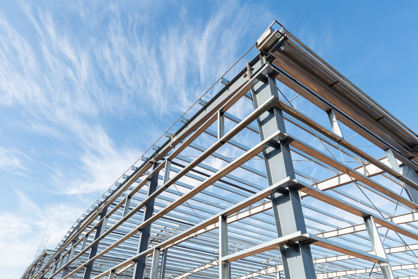 Steel frame structure of a building under construction against a blue sky with scattered clouds.