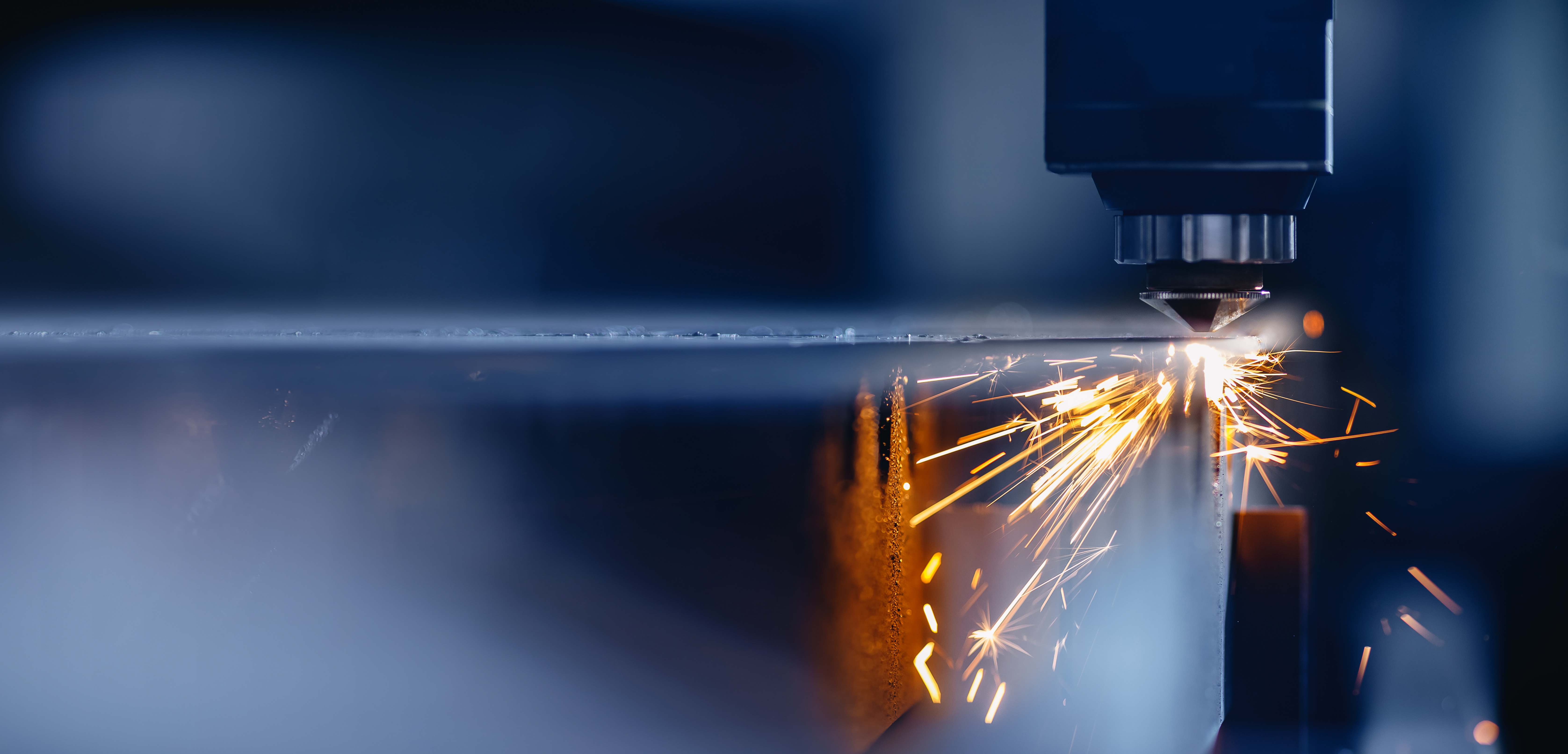 Close-up of a CNC laser cutting machine emitting sparks as it cuts through a sheet of metal in an industrial setting.