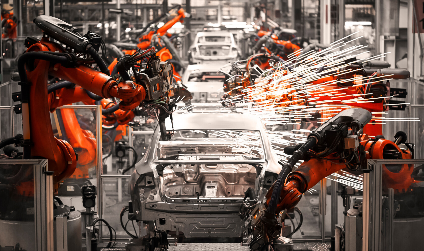 Industrial robots welding and assembling car bodies on a factory production line, with sparks flying in an automotive manufacturing facility.