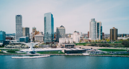 A city skyline with modern and historic buildings is seen along a waterfront on a clear day.